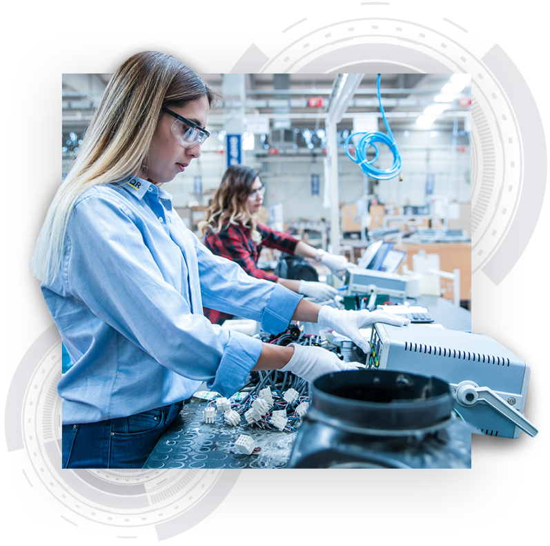 Ein Visual von zwei Frauen, die Elektroteile montieren in einer großen Produktionshalle. Im Hintergrund des Bildes sind zwei hellgraue Designelemente, die ein Präzisionsbauteil darstellen, zu sehen.