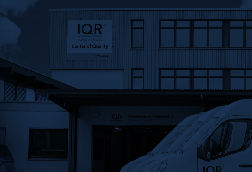 Ein Bildausschnitt vom IQR-Gebäude in Sindelfingen. Vor dem Gebäude stehen drei geparkte IQR-Transporter, die durch den Bildausschnitt nicht ganz zu sehen sind. Das Bild wird von einem dunkelblauen Layer überdeckt.